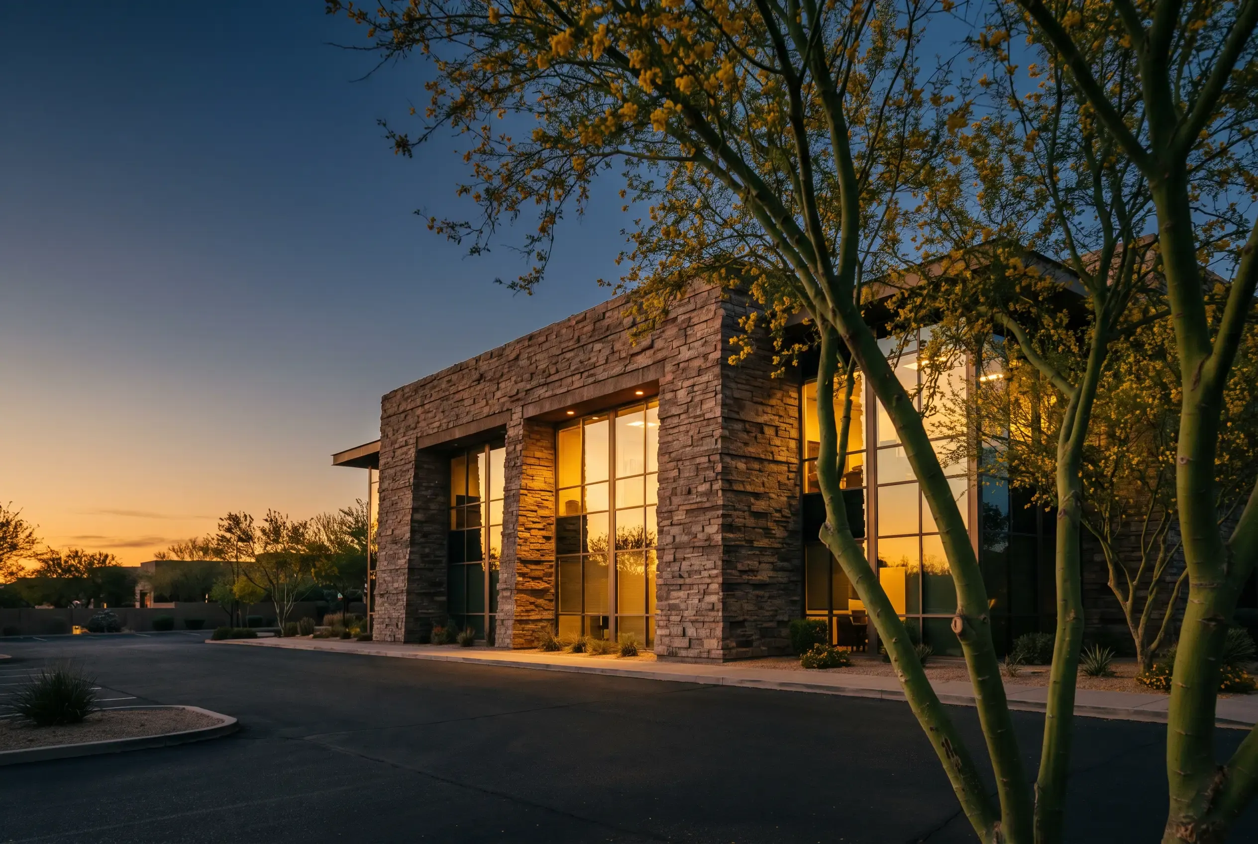 A stone and glass building among desert trees at dusk, lit warmly from inside